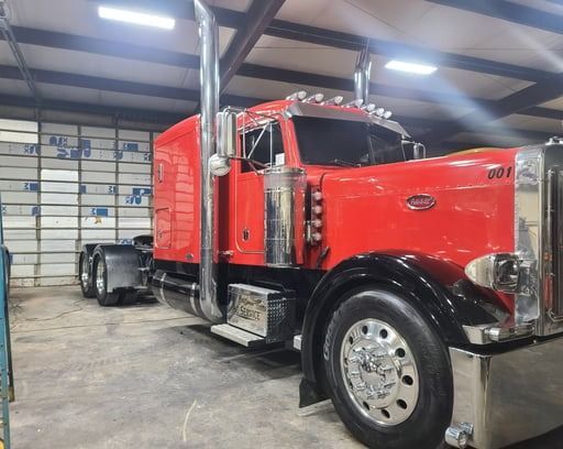Red Peterbilt semi-truck parked inside a building. Chrome accents, black fenders, and dual exhaust pipes.