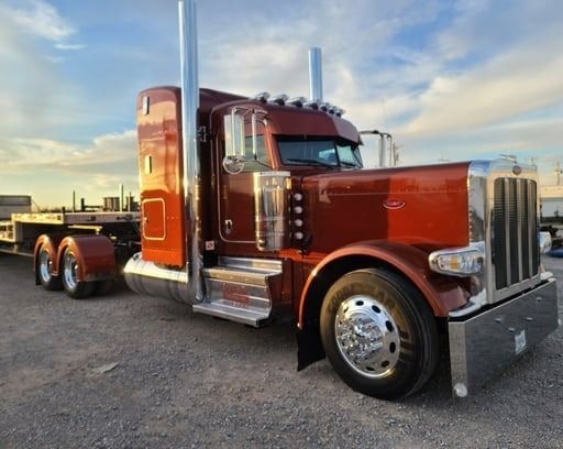 Brown Peterbilt semi-truck with a flatbed trailer parked outdoors on a sunny day.