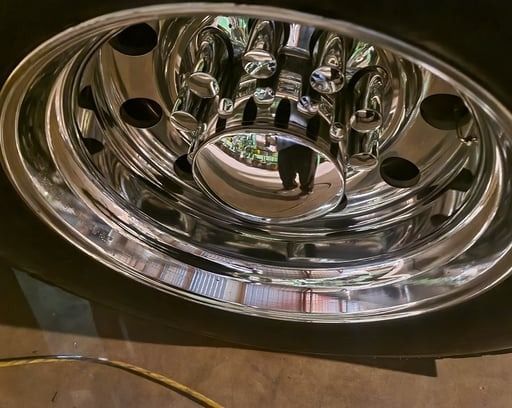 Shiny chrome truck wheel with black tire; reflection of a person.