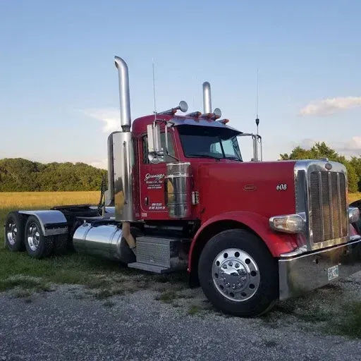 Red semi-truck parked in a grassy field on a sunny day.