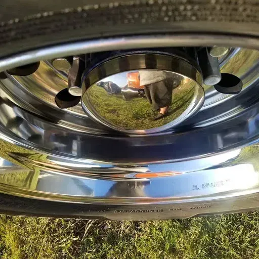Shiny chrome truck wheel with hub cap reflecting a grassy field.