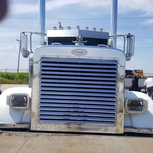 White Peterbilt semi truck with chrome grill and exhaust pipes, parked outdoors.