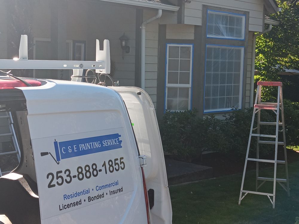 White van with logo parked in front of a house, ladder propped on the lawn, window frame paintng in progress.