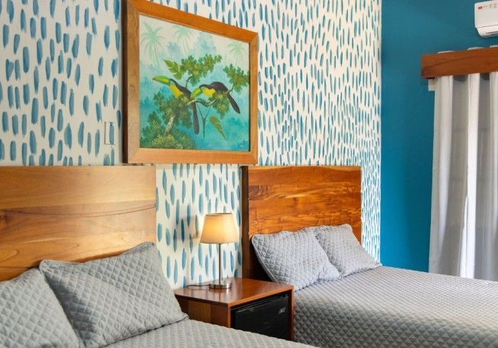 Dos camas en una habitación con cabeceros de madera, arte y papel tapiz con estampado azul.