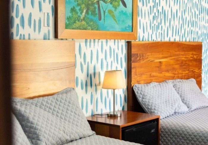 Dos camas con cabeceros de madera y ropa de cama acolchada gris en una habitación con papel pintado azul estampado.