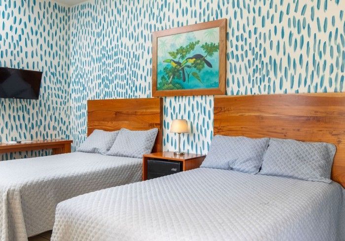 Una habitación de hotel con dos camas, cabeceros de madera y papel tapiz con estampado azul.