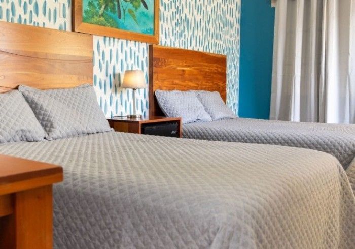 Dos camas queen en una habitación, con cabeceros de madera, colchas grises y papel tapiz estampado.