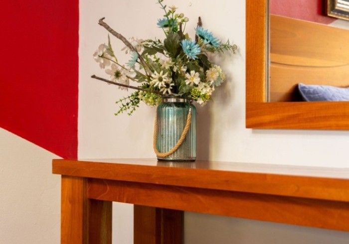 Una mesa de madera con un jarrón de flores frente a una pared roja y blanca y un espejo.