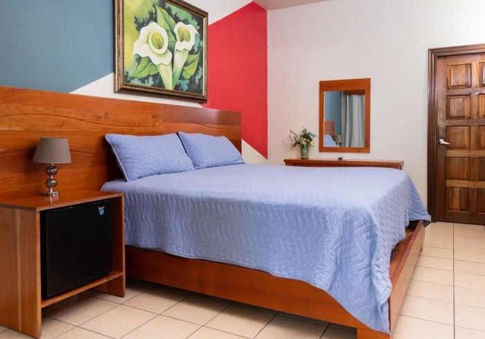 Dormitorio con colcha azul, muebles de madera, obras de arte y una pequeña lámpara.