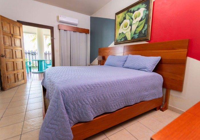 Dormitorio con cama, puerta abierta al balcón, pintura y combinación de colores azul, rojo y blanco.