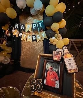 Decoración de cumpleaños para una persona de 55 años con foto, botella, globos negros/dorados y pancarta de Feliz Cumpleaños.