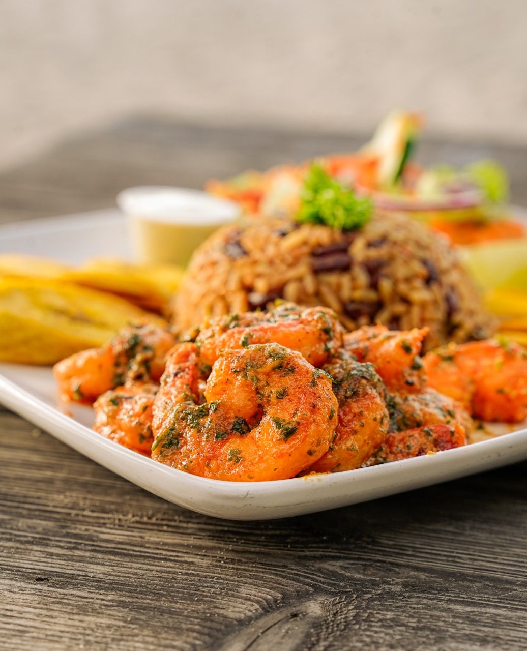 Plato de camarones con arroz, plátanos y ensalada, sobre una mesa de madera.