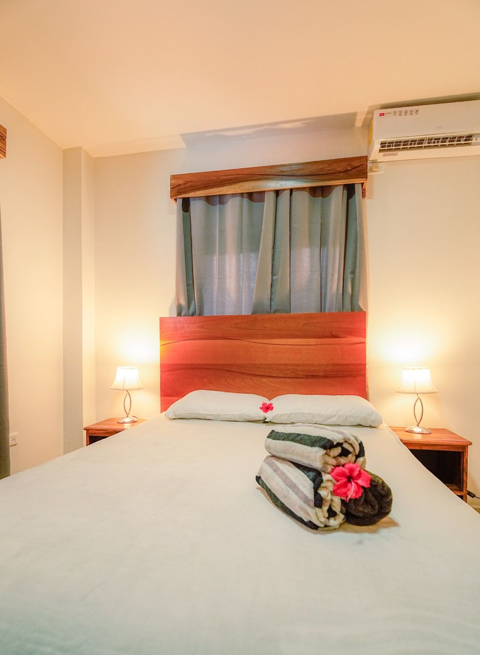 Dormitorio con cama hecha, cabecero de madera, dos mesitas de noche y aparato de aire acondicionado.