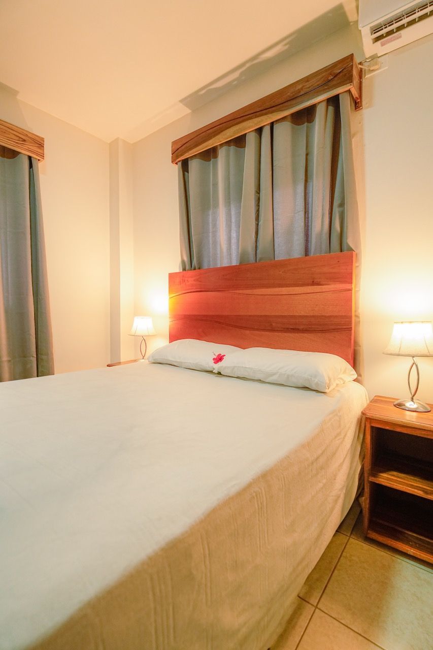 Dormitorio con cama, mesitas de noche, lámparas, cortinas y cabecero de madera.