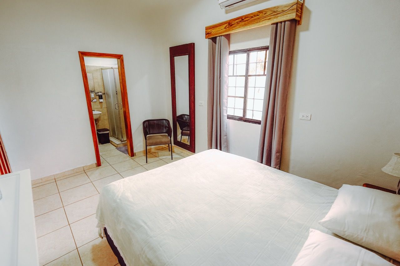 Dormitorio con paredes blancas, una cama, una ventana y una puerta a un baño.