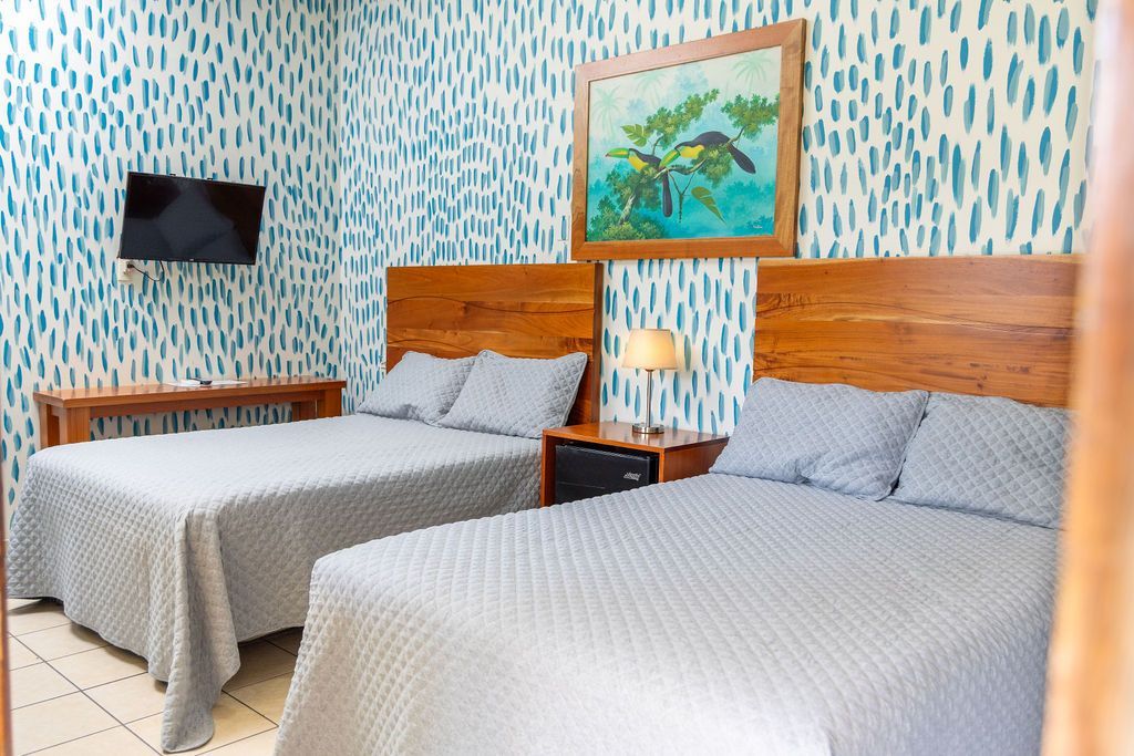 Una habitación de hotel con dos camas, un televisor pequeño y un cuadro en una pared con dibujos azules.