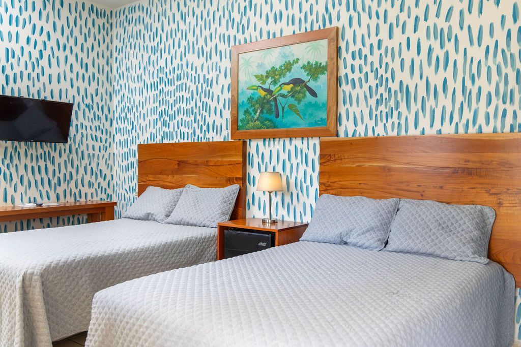 Dos camas tamaño queen en una habitación con papel tapiz y obras de arte con estampados azules.