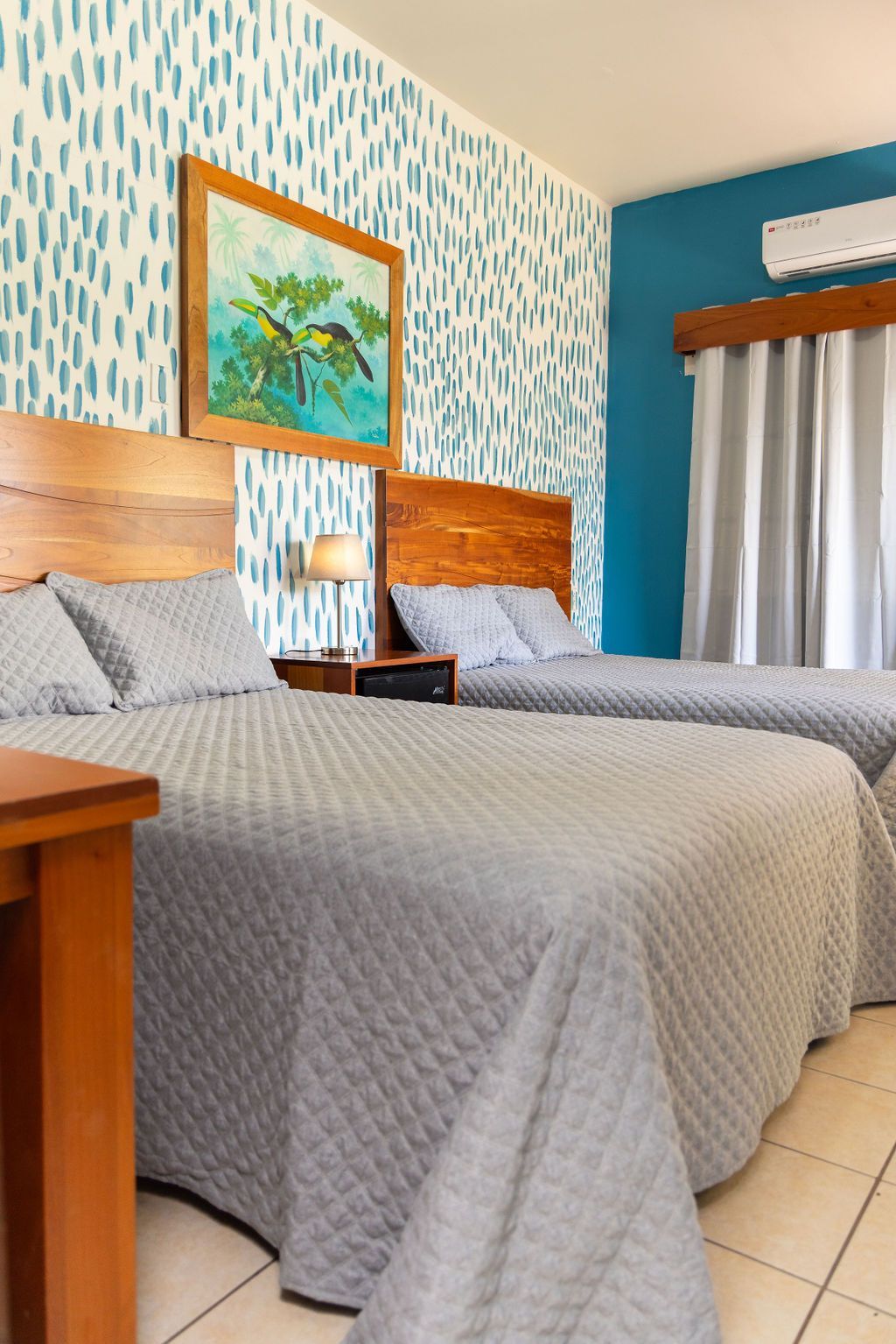 Dormitorio con dos camas cubiertas con edredones grises, una pieza de arte colorida y papel tapiz estampado.