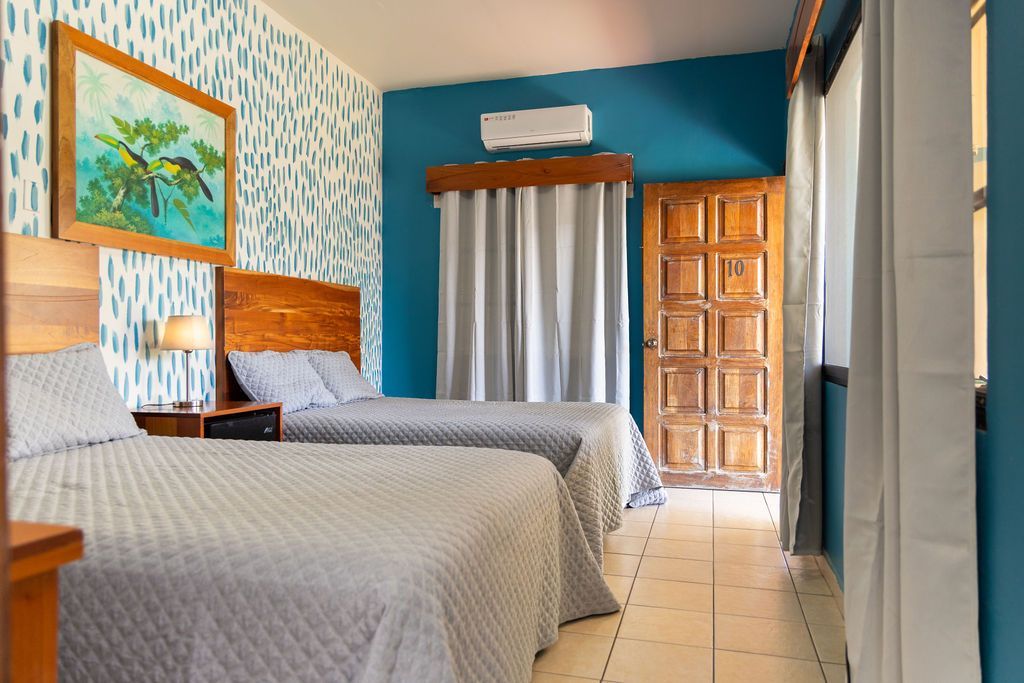 Habitación de hotel con dos camas individuales, paredes azules, una puerta de madera y un cuadro.