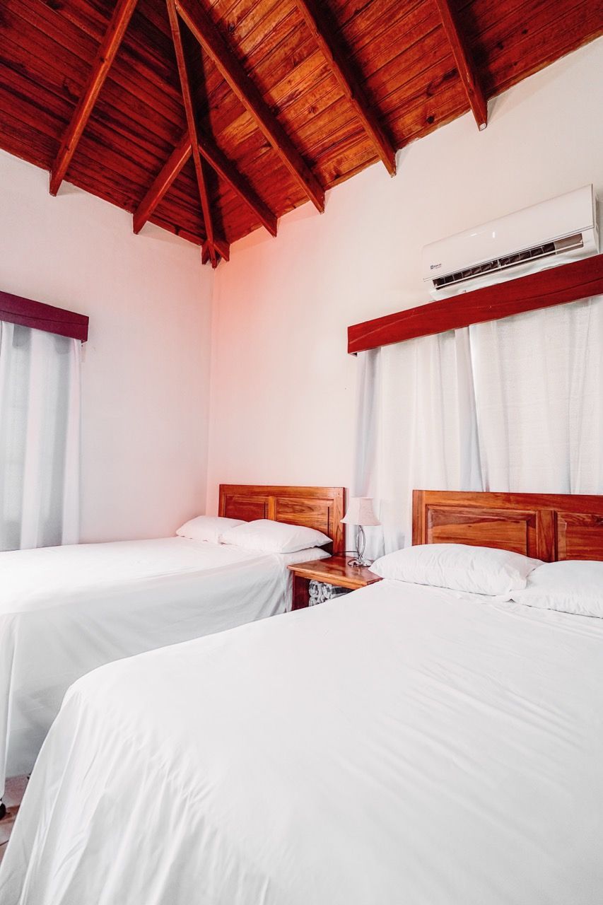 Dormitorio con dos camas, ropa de cama blanca, cabeceros de madera y techo de madera.
