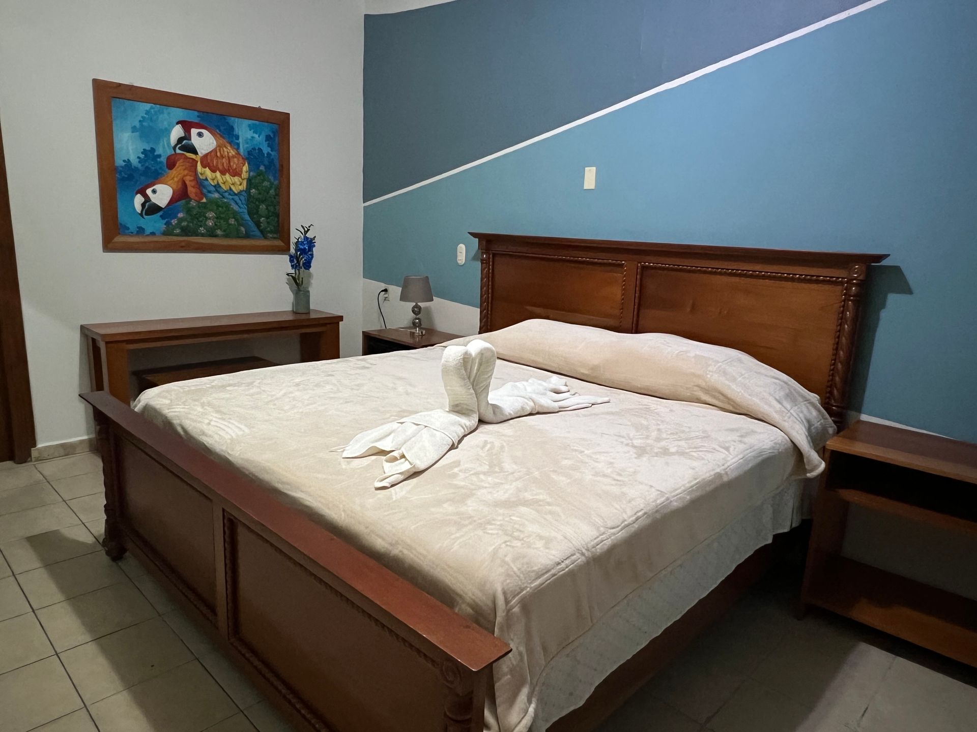 Dormitorio con cama de madera, mesitas de noche y un cuadro colorido en la pared.