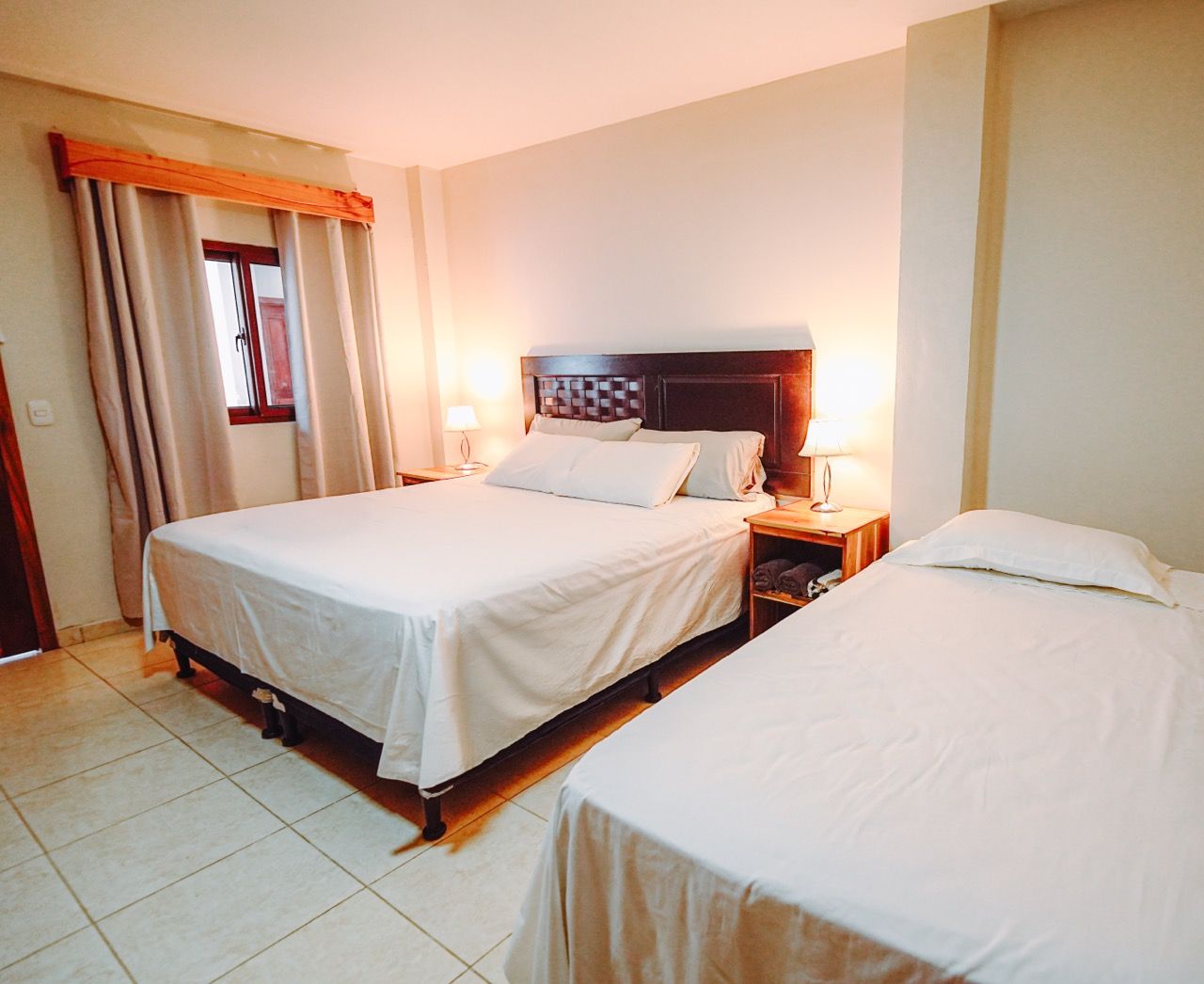 Dormitorio con una cama grande, una cama individual y una ventana con cortinas. Colores neutros.