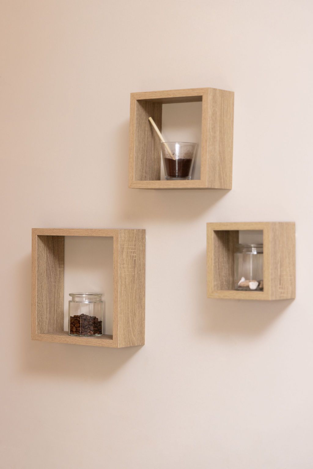 Tres estantes cuadrados de madera sobre una pared beige, cada uno de ellos contiene un frasco de vidrio con su contenido.