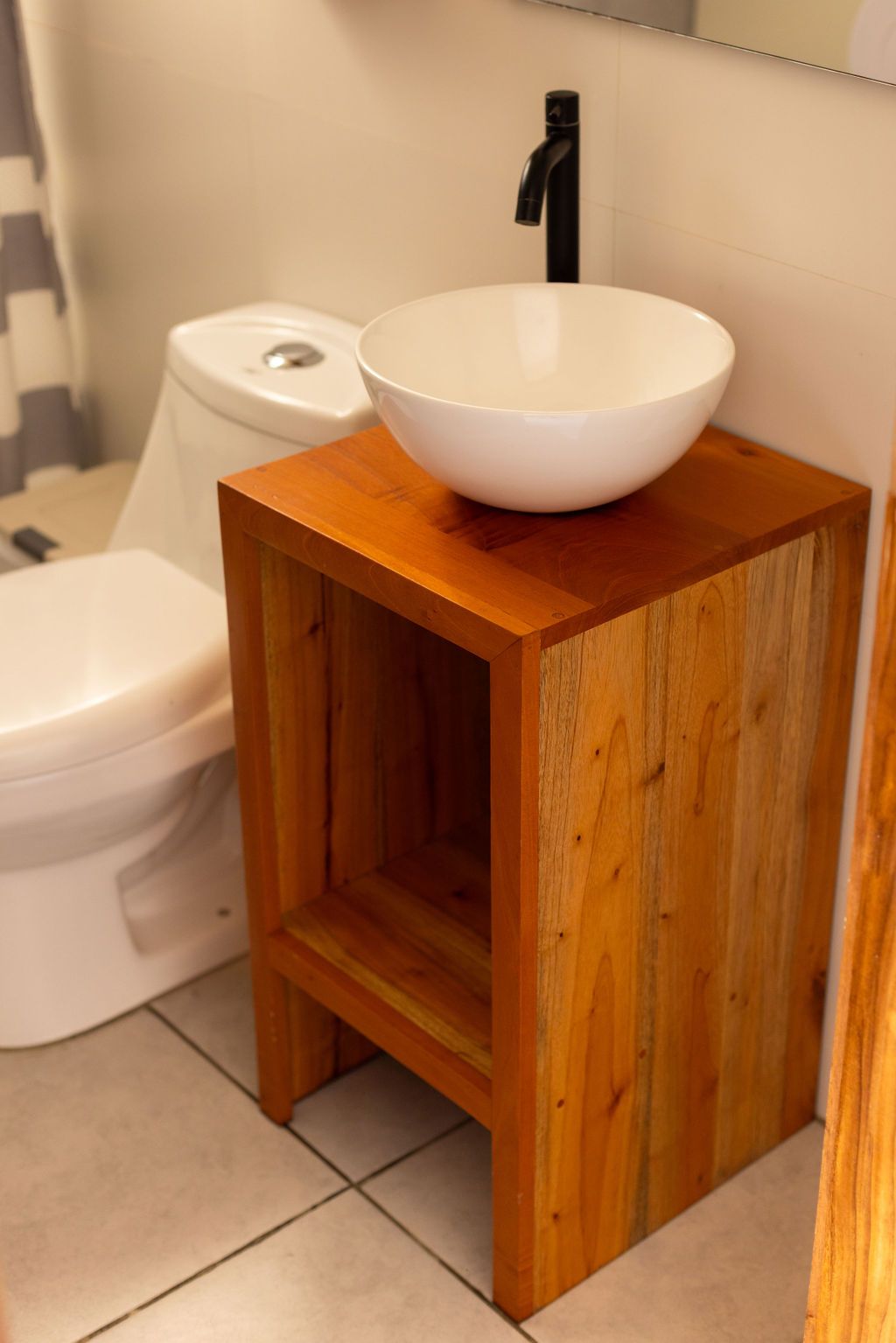 Tocador de madera con lavabo, grifo negro e inodoro en un baño.