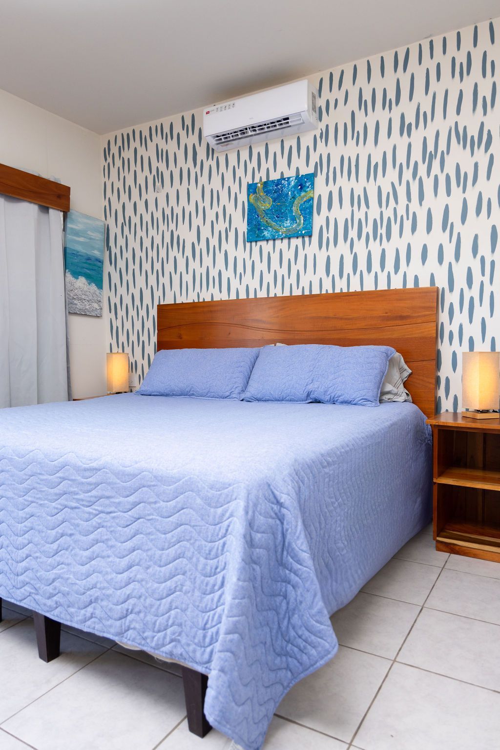Dormitorio con cama, mesita de noche y arte; detalles en azul, cabecera de madera y pared estampada.