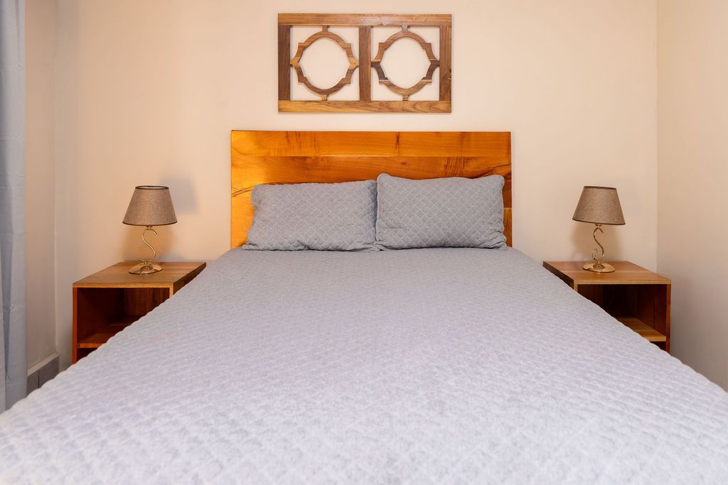 Dormitorio con cabecero de madera, dos mesitas de noche con lámparas y arte decorativo de pared.
