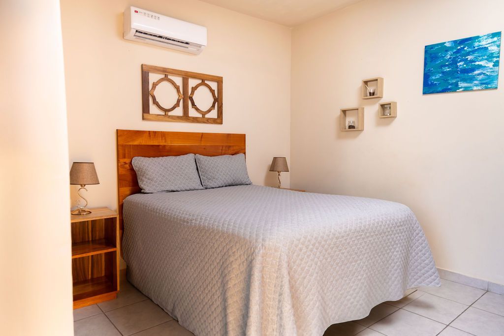 Dormitorio con cama queen, cabecera de madera, mesitas de noche y arte de pared.