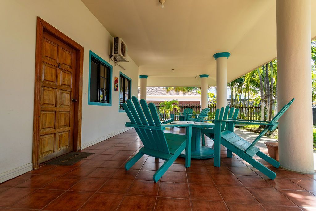Porche al aire libre con sillas color verde azulado, mesa y puerta marrón.