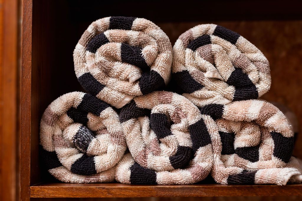 Toallas enrolladas, con estampado de cuadros en tonos tostados y negros, apiladas dentro de un estante de madera.