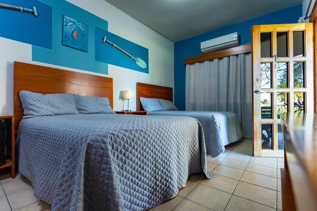 Dos camas queen en una habitación con detalles azules y una puerta al exterior.