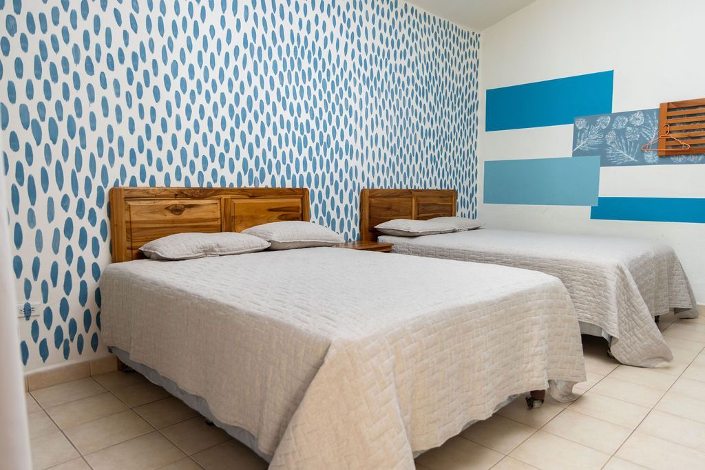 Dos camas en una habitación, con papel tapiz y detalles estampados en azul y blanco.