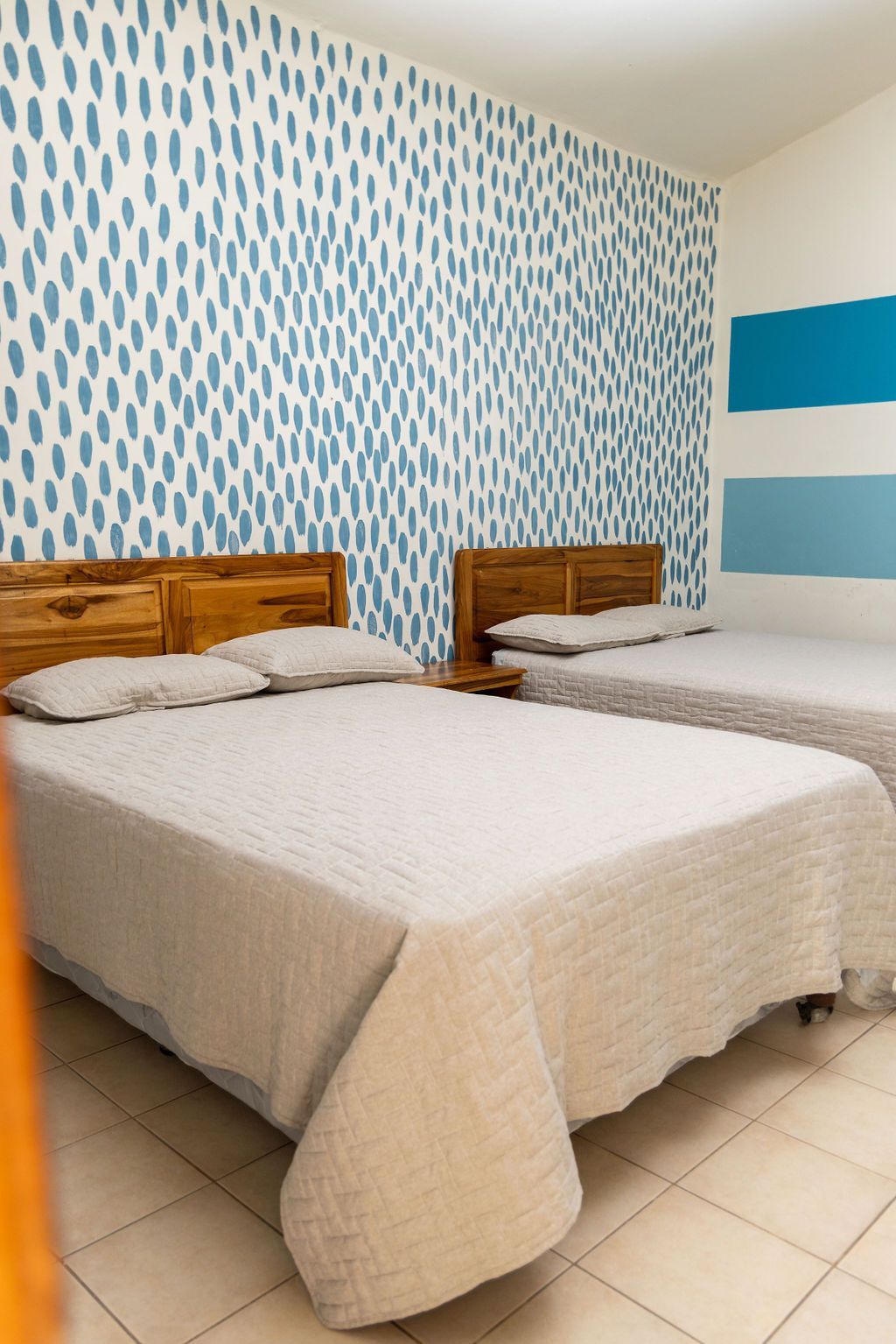 Dormitorio con dos camas, cabeceros de madera, ropa de cama blanca y pared estampada en azul y blanco.