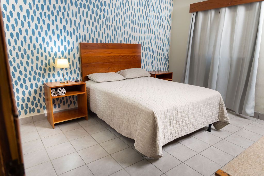 Dormitorio con estructura de cama de madera, mesitas de noche y una pared con acento estampado en azul.