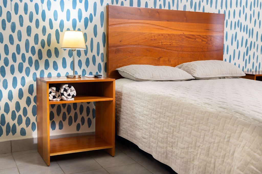 Dormitorio de madera con cama, mesita de noche y pared estampada en azul y blanco.
