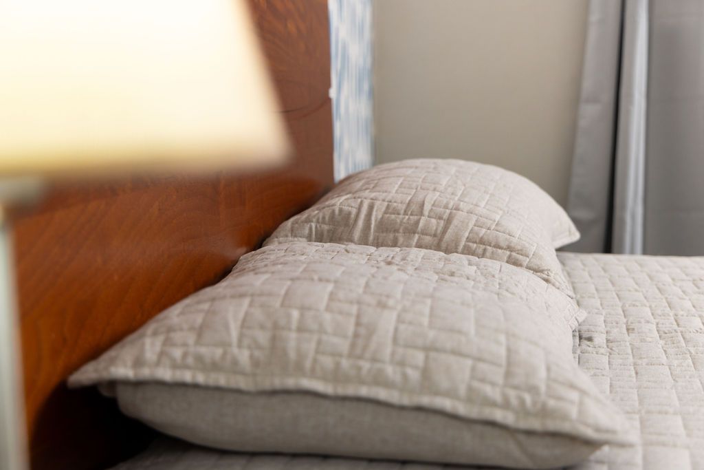 Dos almohadas beige sobre una cama acolchada, con un cabecero marrón y una lámpara en primer plano.