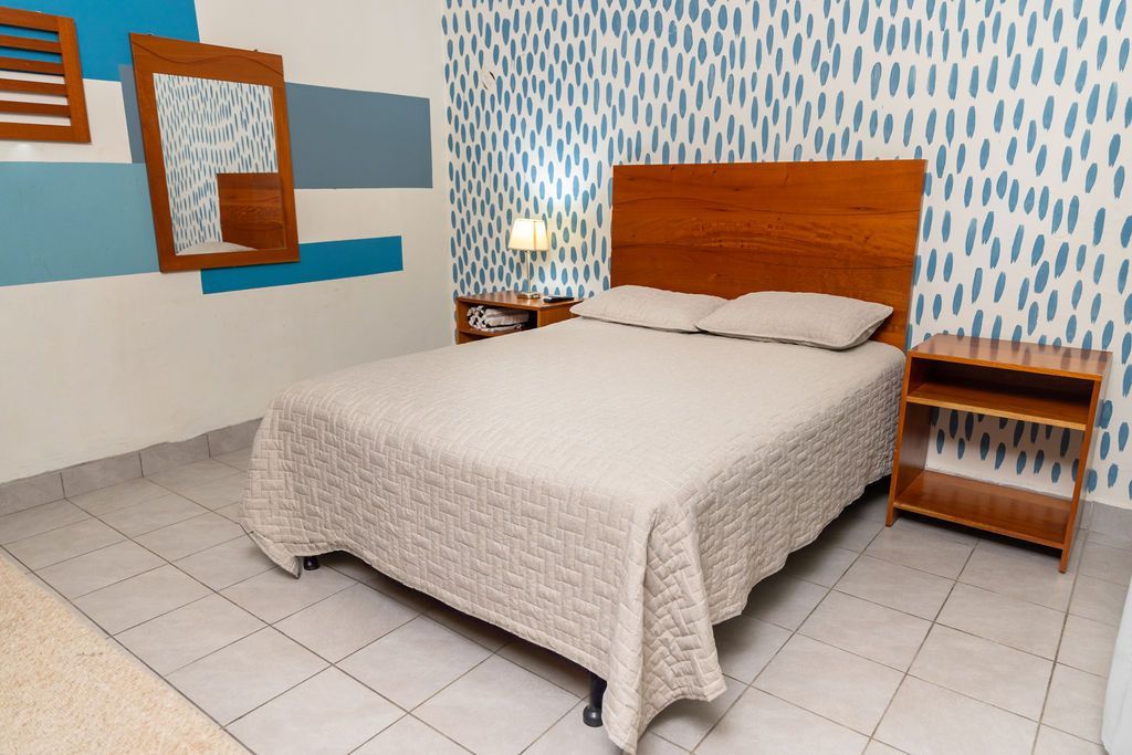 Dormitorio con cama, mesitas de noche, cabecero de madera y pared con estampado azul y blanco.