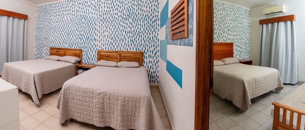 Habitación de hotel con tres camas, papel tapiz estampado y detalles en madera.