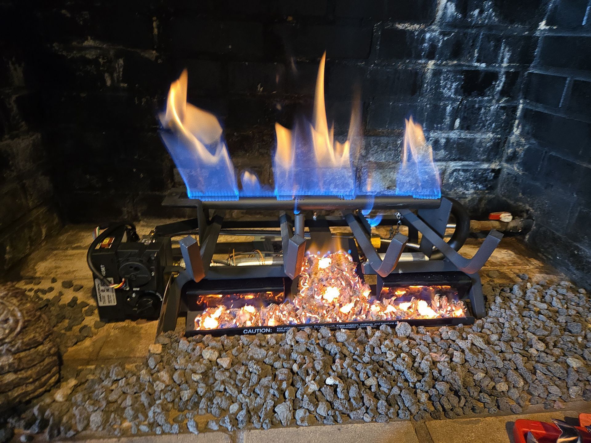 A gas fireplace with blue and orange flames burning above glowing embers.