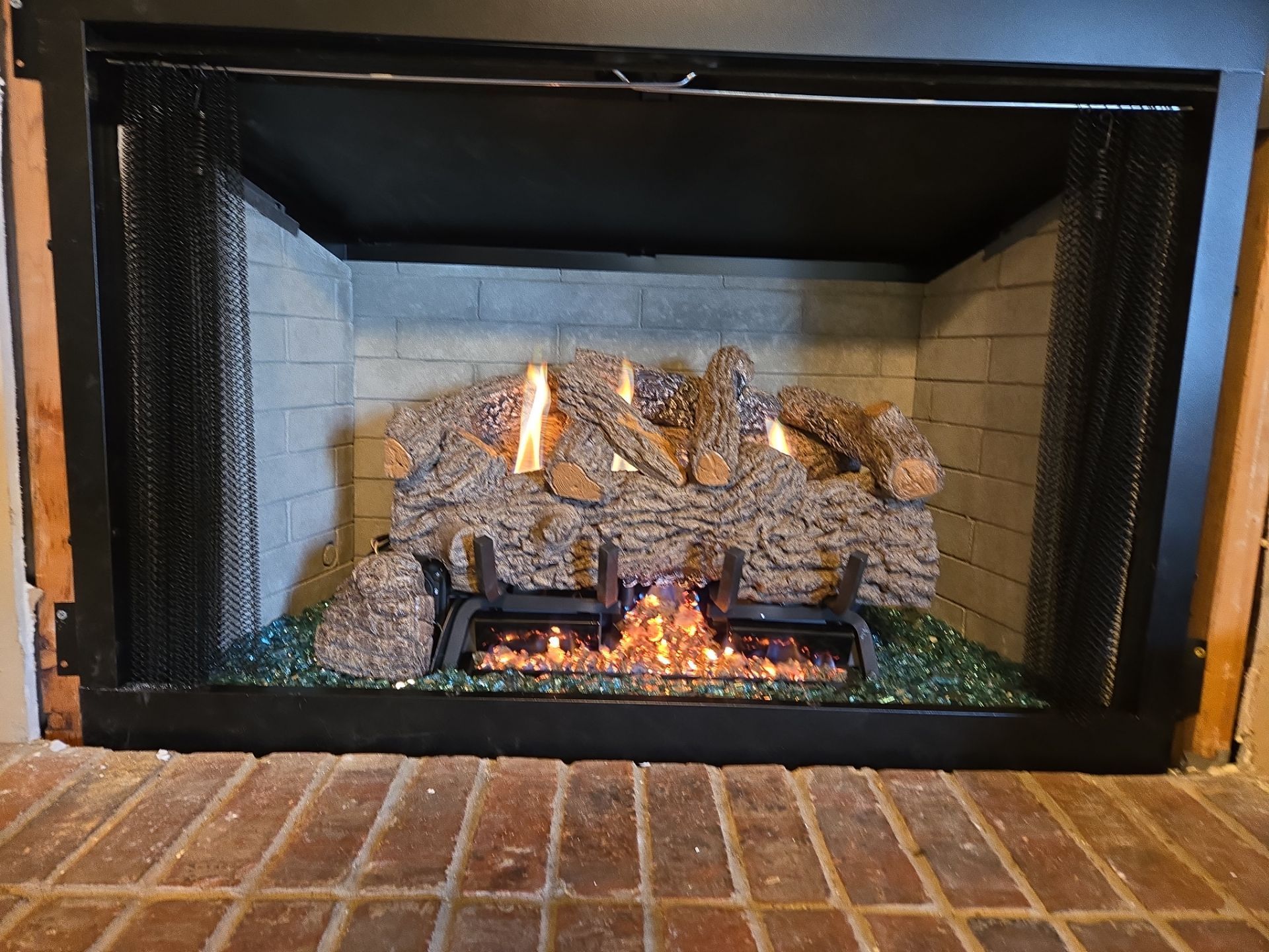 Fireplace with a gas fire, logs, and a protective screen.
