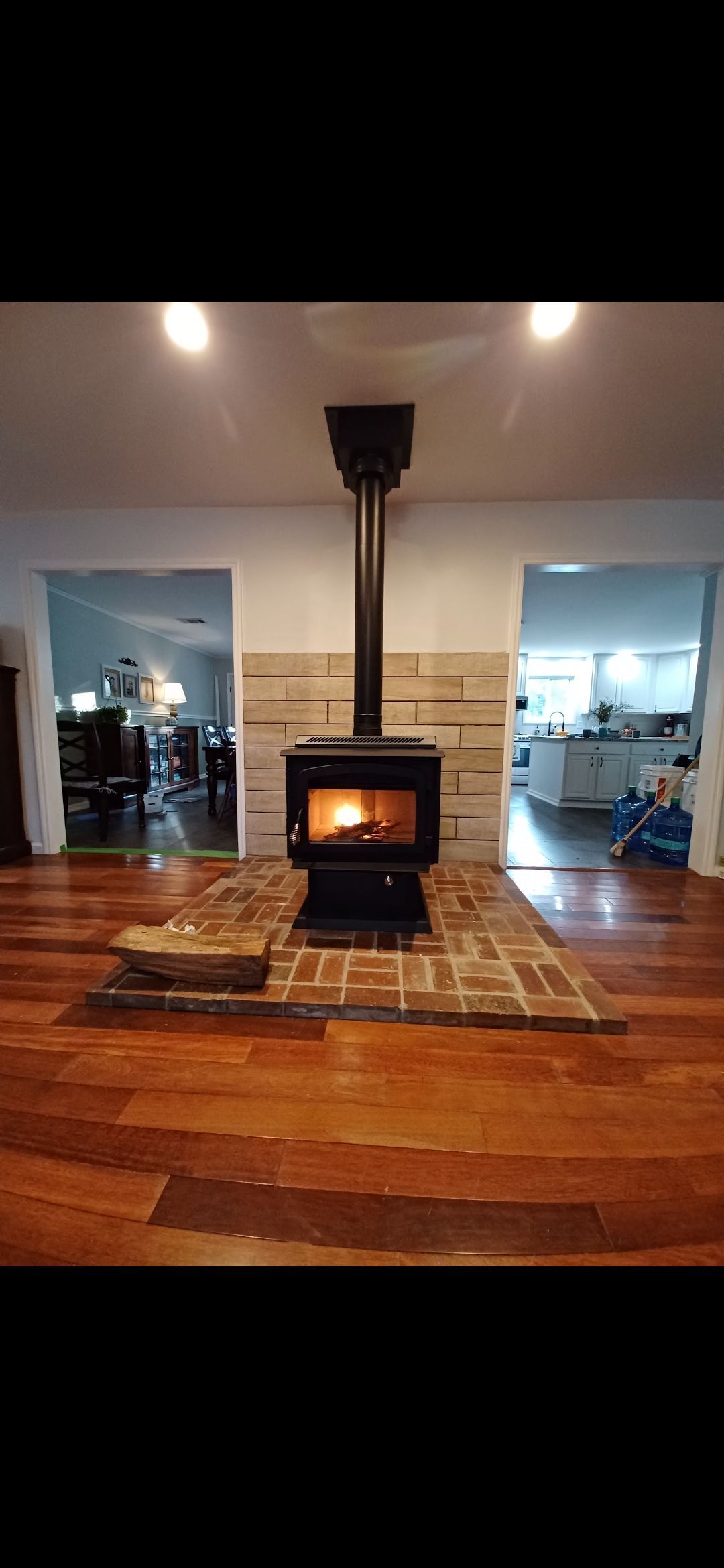 A wood-burning stove with a lit fire sits on a brick hearth. Two open doorways flank the stove.