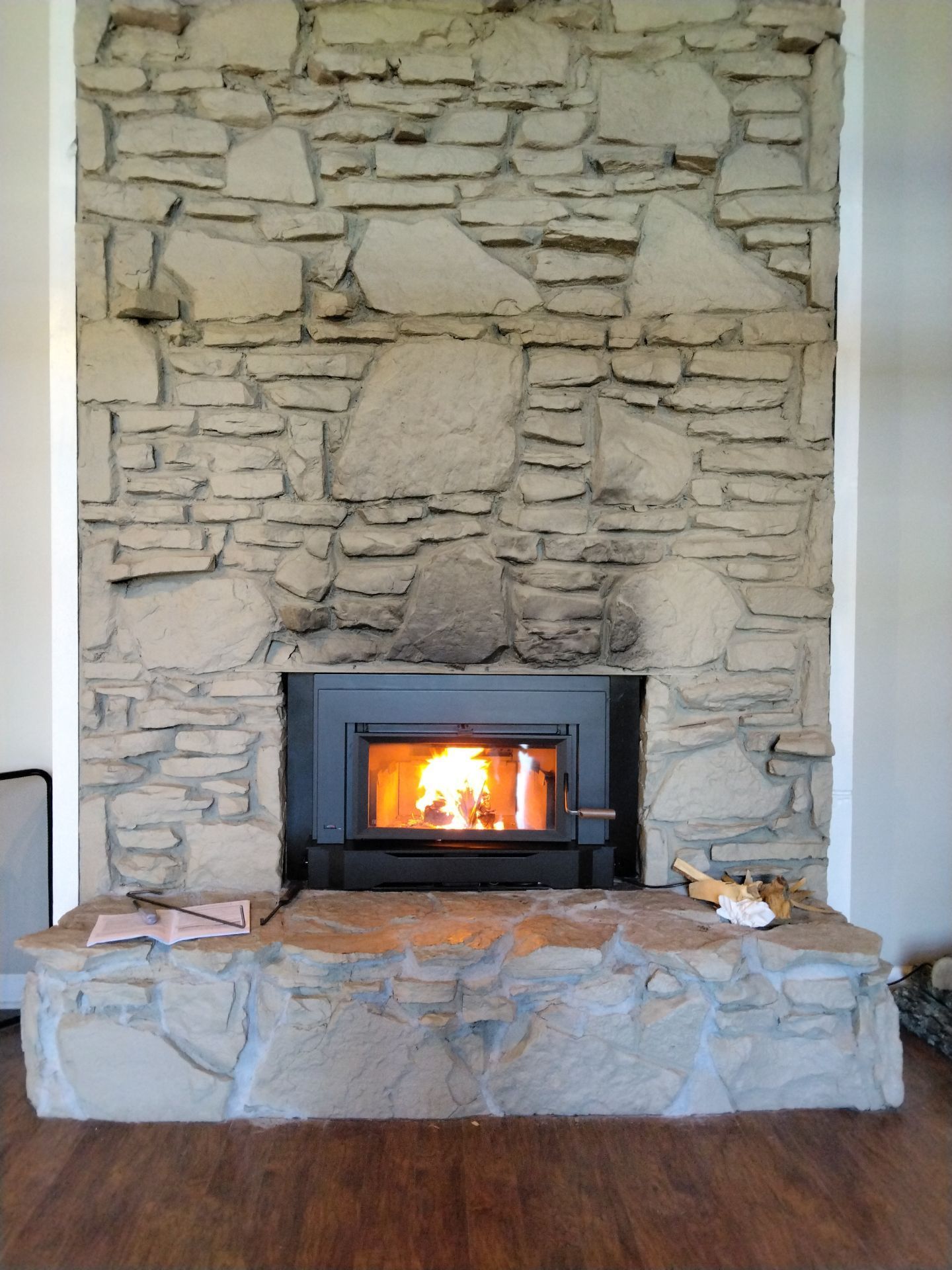 Fireplace with stone facade, fire burning inside. Wood floor, with white trim around the fireplace.