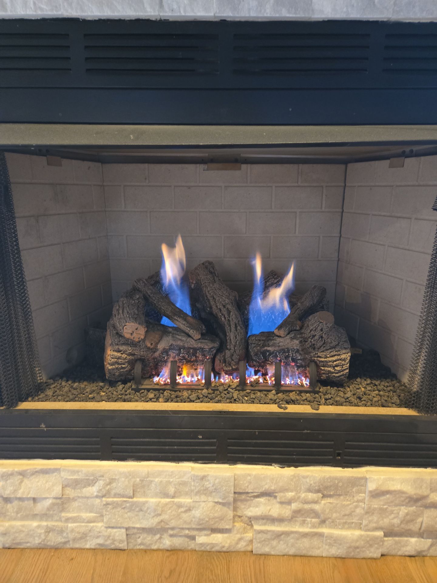 Gas fireplace with blue flames and dark logs burning in a white brick hearth.