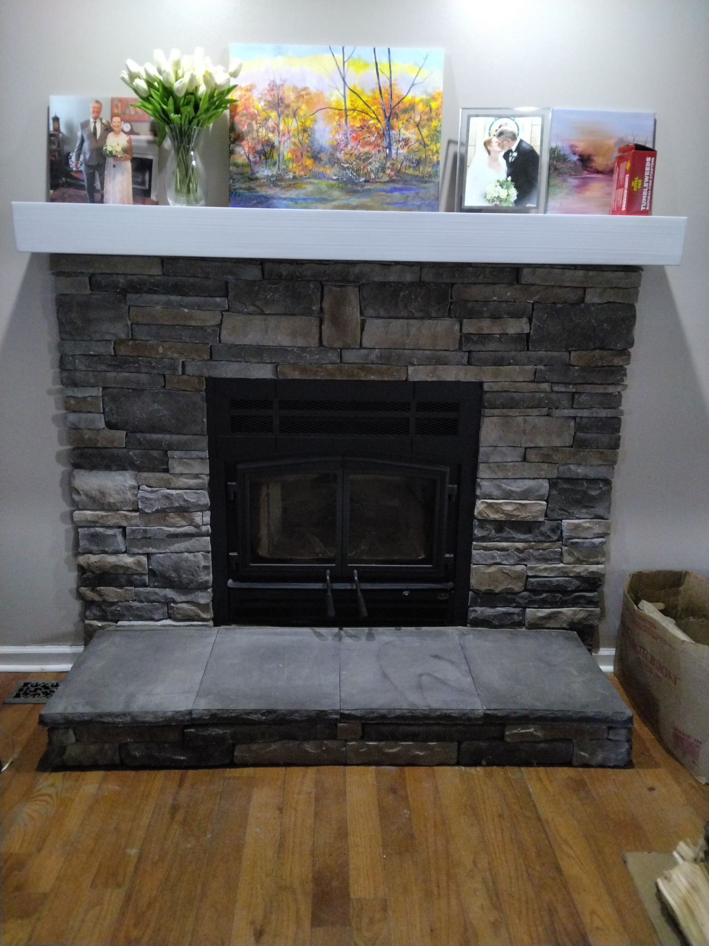 Stone fireplace with white mantel, artwork, flowers, and photos.
