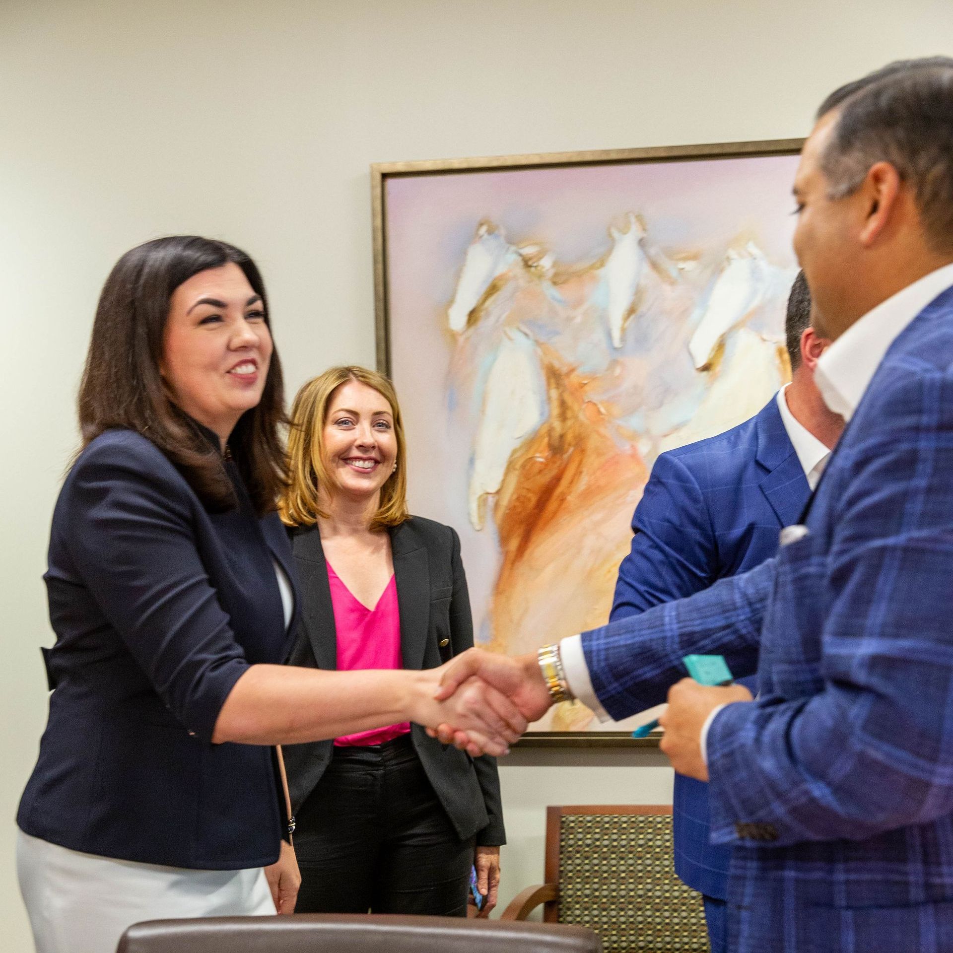 A group of people shaking hands in front of a painting of horses