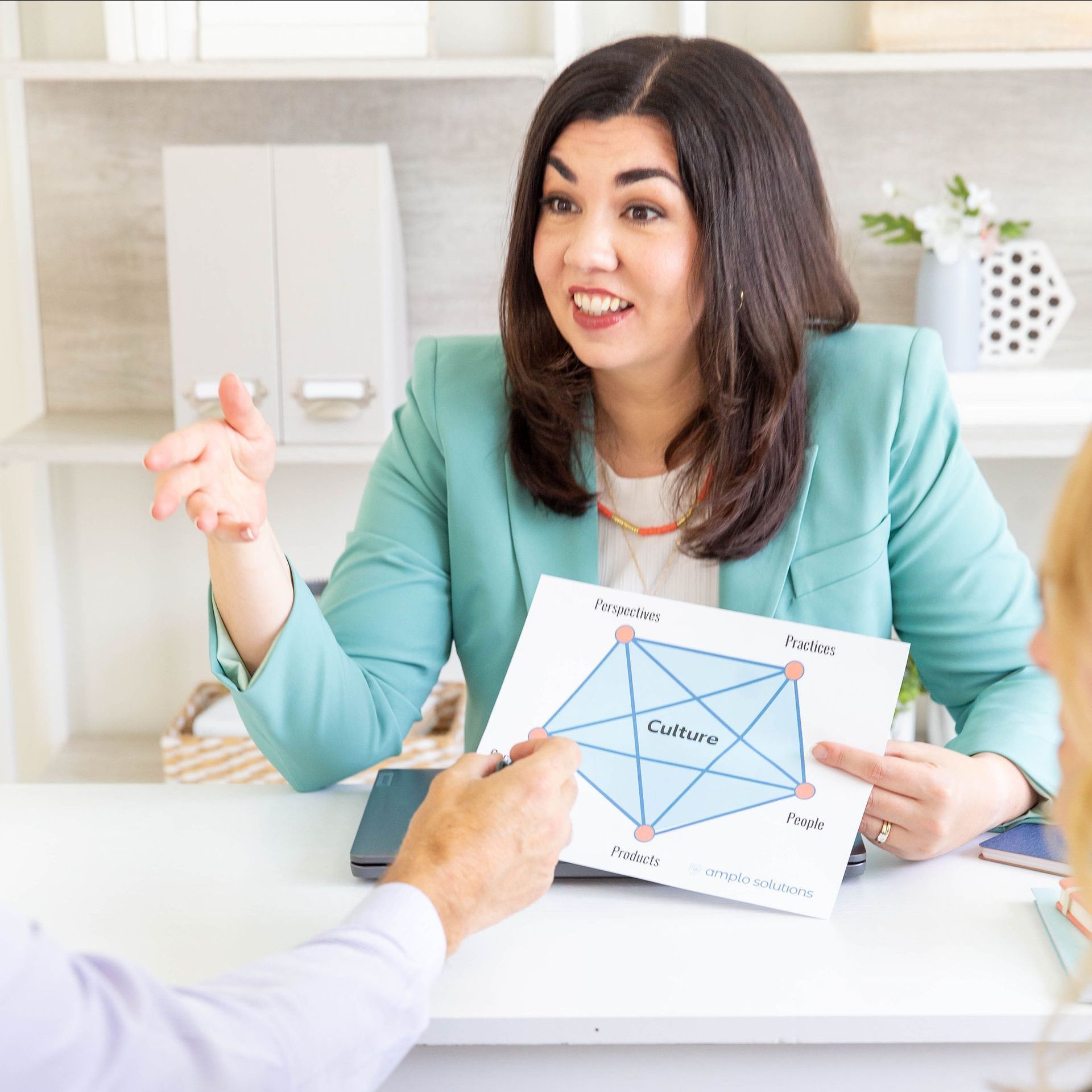 A woman is sitting at a table holding a piece of paper and talking to a man.