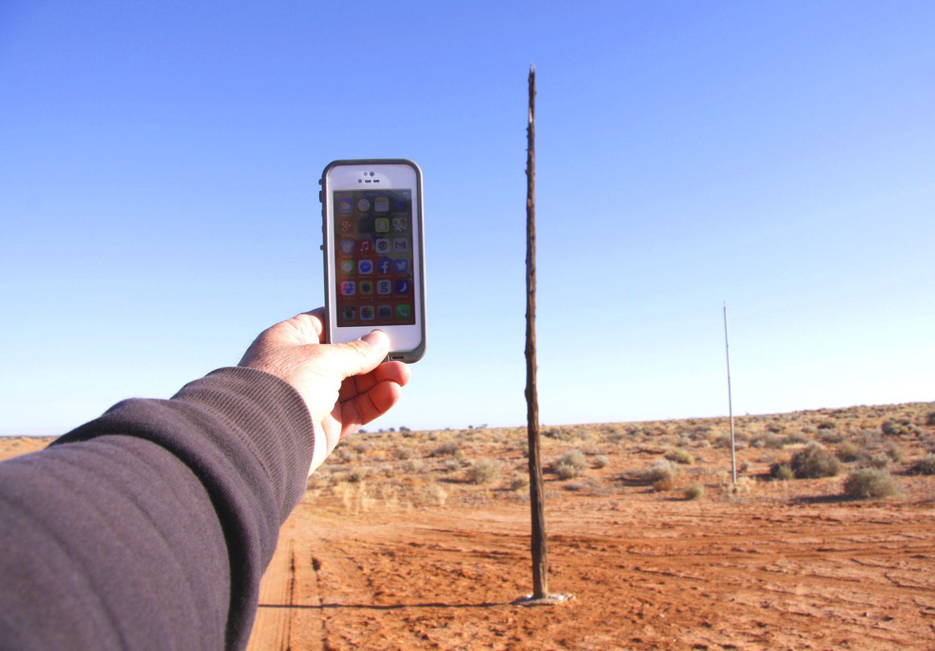 A modern cell phone is held up in front of an old telegraph pole in the Australian Outback. The cell phone is a stark contrast to the old telegraph pole, which is a reminder of the past. The image captures the juxtaposition of old and new technology in the Australian Outback.